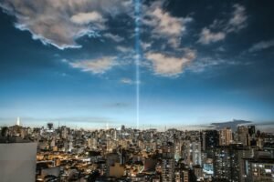 Panoramic view of Sao Paulo's urban skyline at twilight with a striking light beam amidst clouds.