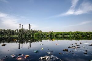 View of a polluted river reflecting factory emissions under a clear sky in India.