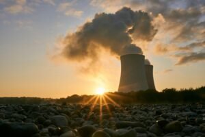 A nuclear power plant emitting steam at sunrise, creating a dramatic skyline with visible air pollution.